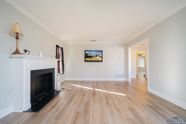 unfurnished living room with a tiled fireplace, crown molding, and light wood-type flooring