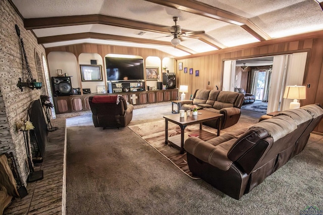 living room with wood walls, lofted ceiling with beams, ceiling fan, a textured ceiling, and carpet floors