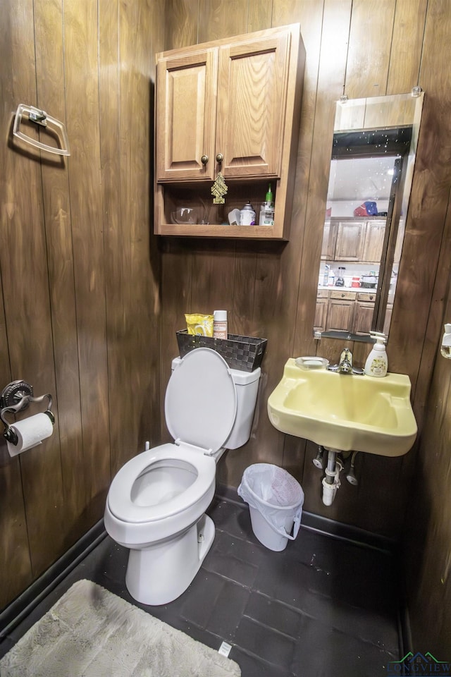 bathroom with tile patterned floors, toilet, wooden walls, and sink