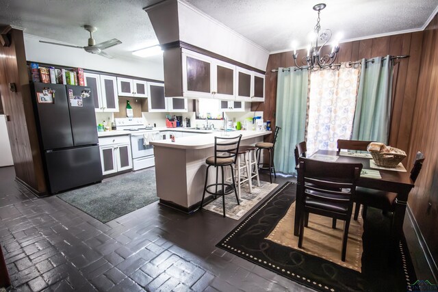 kitchen featuring kitchen peninsula, stainless steel fridge, white electric range oven, a textured ceiling, and wood walls