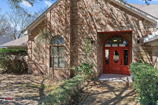 property entrance with a shingled roof and brick siding