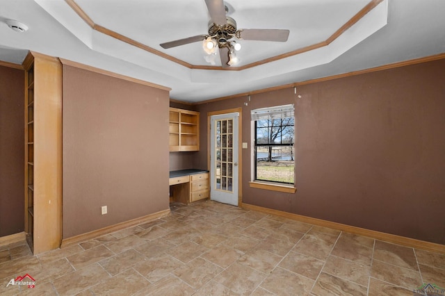 unfurnished bedroom featuring a tray ceiling, built in study area, and baseboards