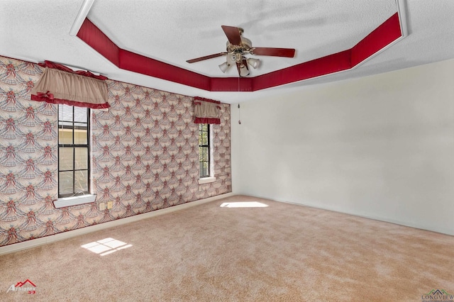 unfurnished room featuring a textured ceiling, ceiling fan, a tray ceiling, and carpet