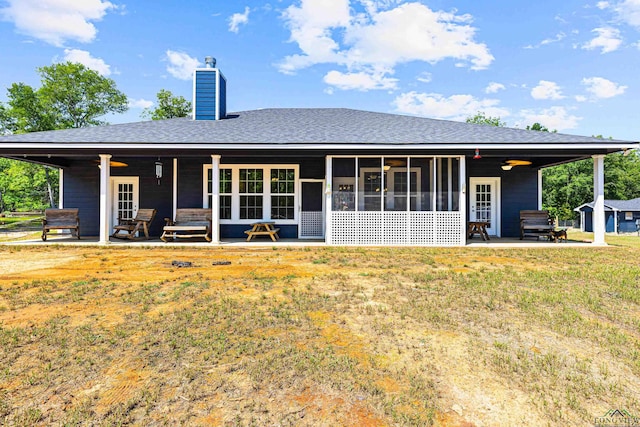 back of property with a shingled roof, a lawn, a sunroom, a chimney, and a patio area