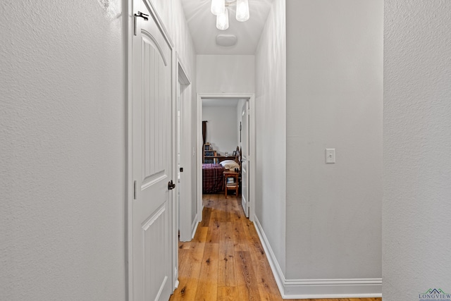 hallway with a textured wall, light wood-style flooring, and baseboards