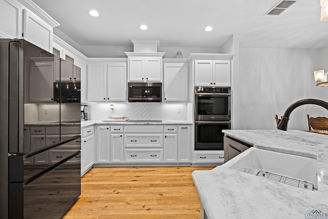 kitchen with stainless steel appliances, visible vents, light wood-style flooring, white cabinets, and a sink