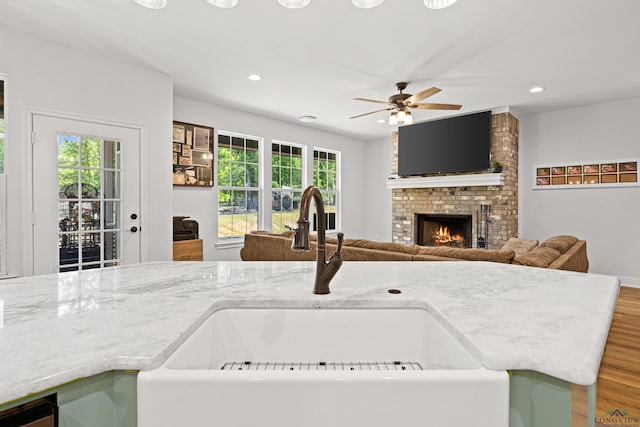 kitchen featuring recessed lighting, wood finished floors, a sink, open floor plan, and a brick fireplace