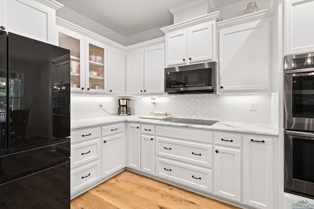 kitchen with black appliances, light stone counters, glass insert cabinets, and white cabinets