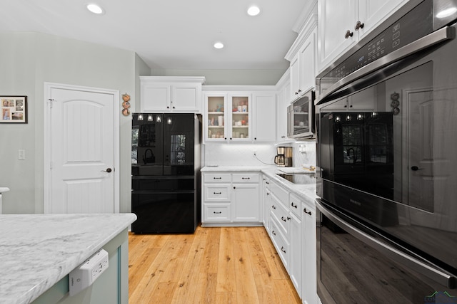 kitchen featuring light wood-style flooring, glass insert cabinets, stainless steel microwave, freestanding refrigerator, and white cabinetry