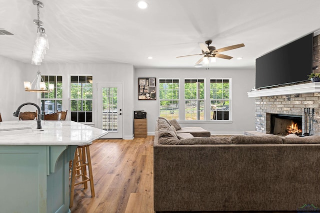 living area featuring visible vents, light wood-style floors, ceiling fan with notable chandelier, a brick fireplace, and recessed lighting