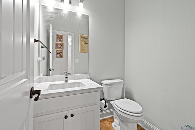 half bathroom featuring a textured wall, toilet, wood finished floors, vanity, and baseboards