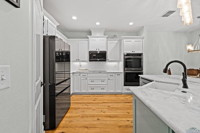 kitchen featuring light wood finished floors, appliances with stainless steel finishes, hanging light fixtures, white cabinetry, and a sink