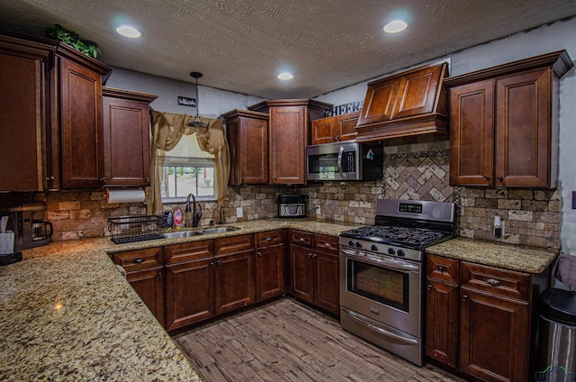 kitchen with hanging light fixtures, sink, light wood-type flooring, appliances with stainless steel finishes, and custom range hood