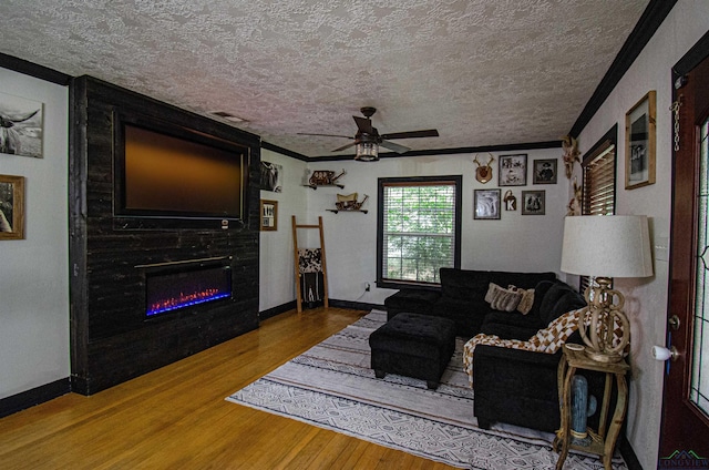 living room with ceiling fan, a large fireplace, crown molding, wood-type flooring, and a textured ceiling