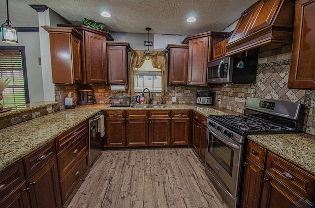 kitchen featuring a textured ceiling, stainless steel appliances, sink, light hardwood / wood-style flooring, and hanging light fixtures