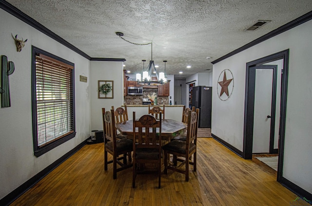 dining space with hardwood / wood-style flooring, a textured ceiling, crown molding, and an inviting chandelier