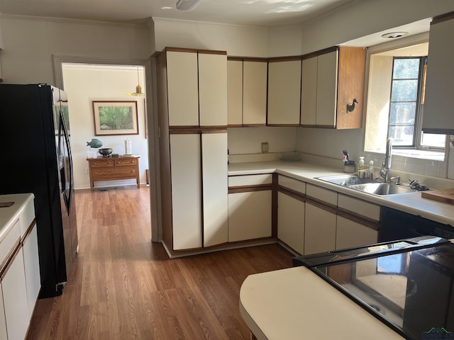 kitchen with stove, black fridge, sink, cream cabinetry, and dark hardwood / wood-style floors