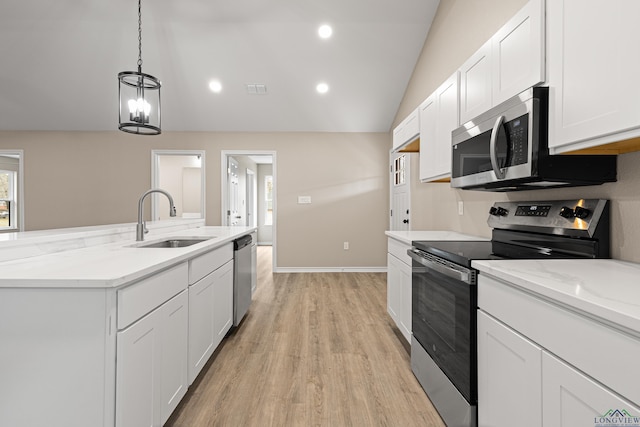 kitchen with light wood finished floors, a sink, vaulted ceiling, appliances with stainless steel finishes, and white cabinetry