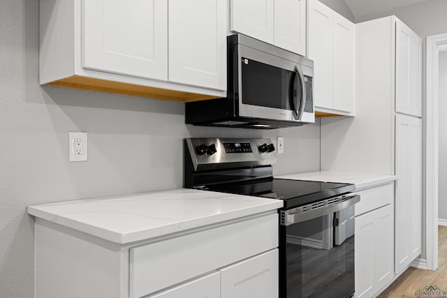 kitchen featuring light wood-type flooring, light stone countertops, appliances with stainless steel finishes, and white cabinetry