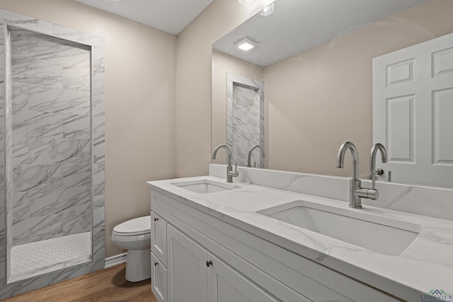 full bathroom featuring a sink, tiled shower, toilet, and wood finished floors