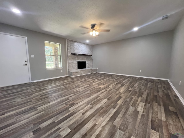 unfurnished living room with dark hardwood / wood-style flooring, a large fireplace, a textured ceiling, and ceiling fan