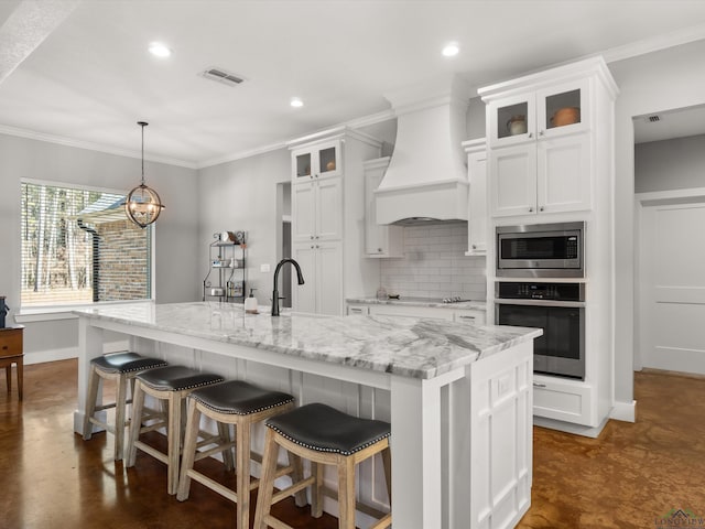 kitchen with white cabinetry, custom range hood, a kitchen island with sink, and appliances with stainless steel finishes