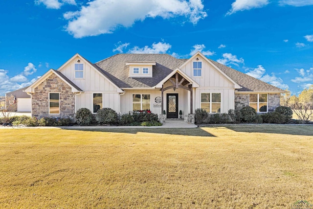 view of front facade featuring board and batten siding, a front yard, stone siding, and a shingled roof