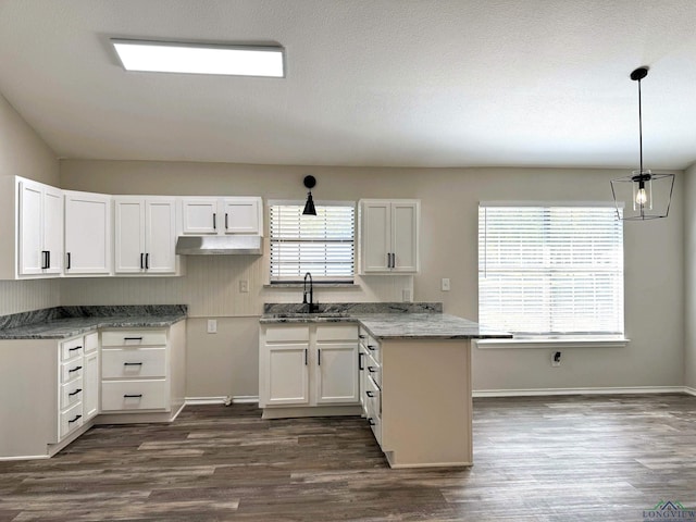 kitchen with sink, white cabinetry, stone counters, hanging light fixtures, and a wealth of natural light