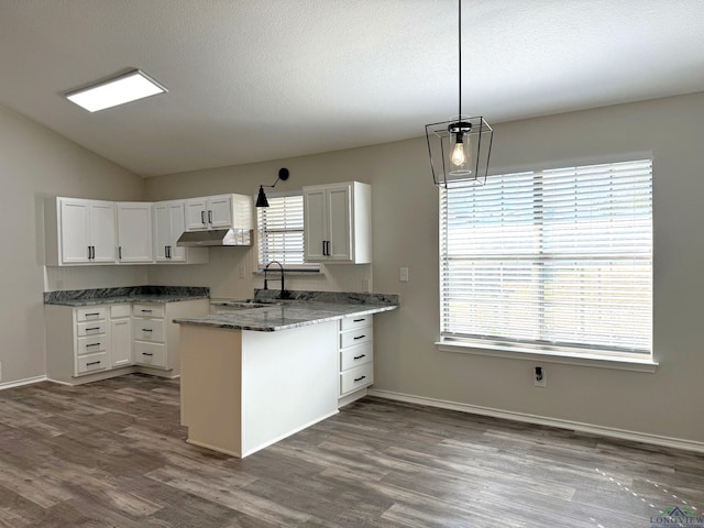 kitchen featuring decorative light fixtures, vaulted ceiling, dark stone countertops, kitchen peninsula, and white cabinets