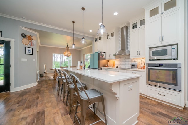 10740 Fm 2685, Gladewater, TX 75647 - kitchen featuring appliances with stainless steel finishes, wall chimney range hood, ornamental molding, tasteful backsplash, and a center island with sink