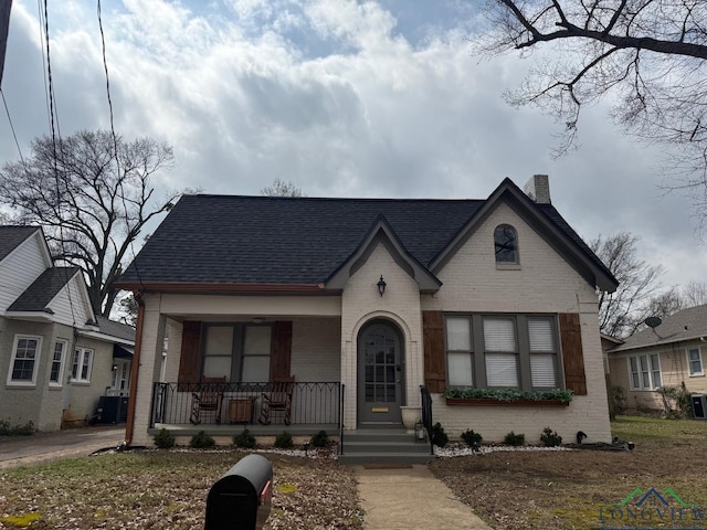 view of front of home featuring brick siding, covered porch, roof with shingles, and a chimney