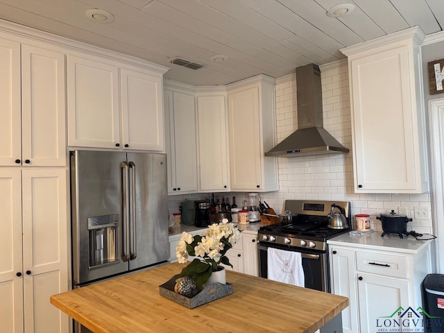 kitchen with wall chimney range hood, tasteful backsplash, appliances with stainless steel finishes, and wood counters