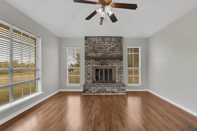 unfurnished living room with a textured ceiling, hardwood / wood-style flooring, a brick fireplace, and ceiling fan