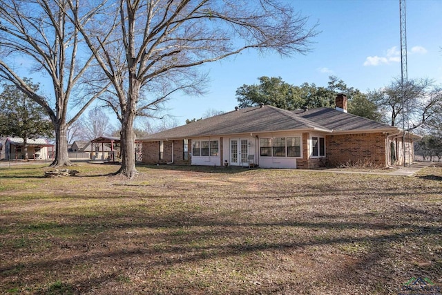 back of house featuring a chimney, a lawn, french doors, and brick siding