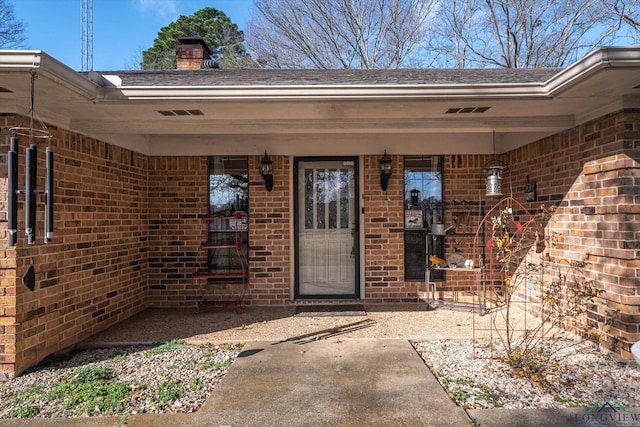 view of exterior entry with a chimney and brick siding