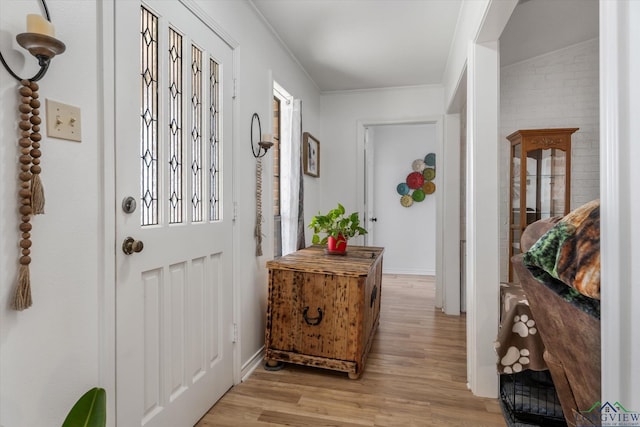 doorway to outside featuring light wood-type flooring, baseboards, and crown molding