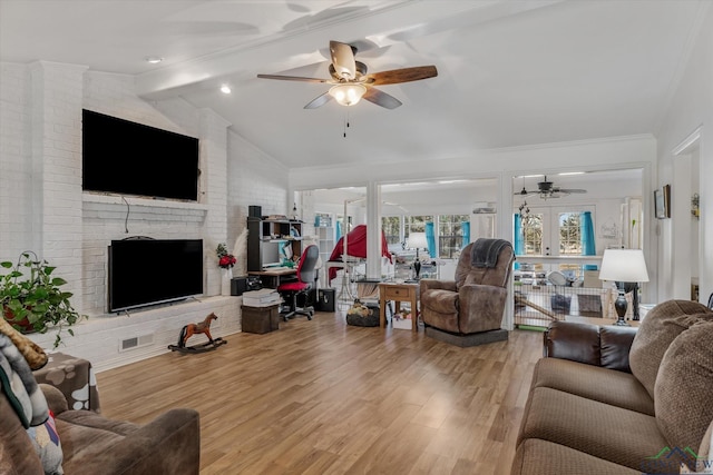 living room with lofted ceiling with beams, a brick fireplace, light wood-style flooring, and ceiling fan