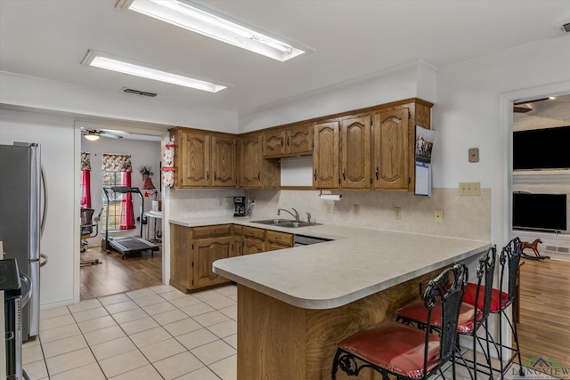 kitchen with a peninsula, stainless steel appliances, brown cabinets, and light countertops