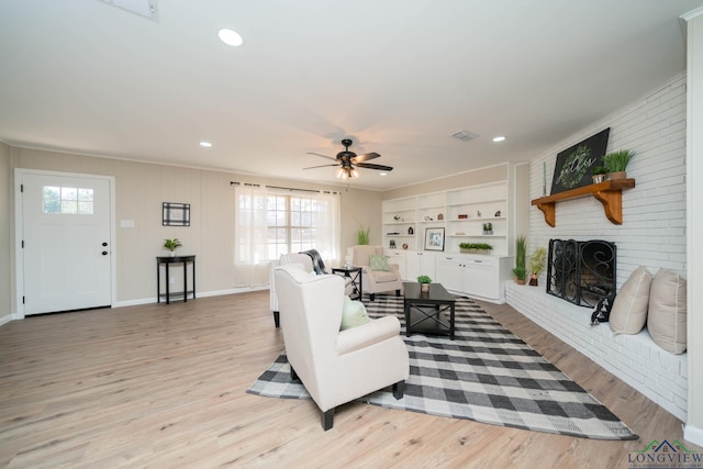 living room with built in features, a fireplace, light hardwood / wood-style floors, and ceiling fan