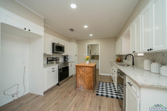 kitchen with sink, light hardwood / wood-style flooring, appliances with stainless steel finishes, white cabinetry, and light stone counters