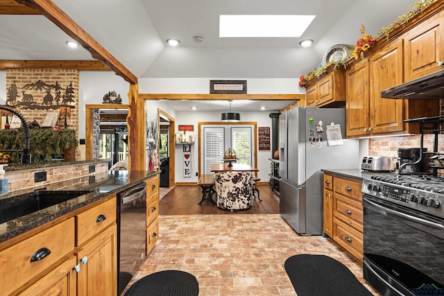 kitchen with sink, stainless steel appliances, backsplash, dark stone counters, and vaulted ceiling with skylight