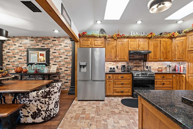 kitchen with dark stone counters, black range, vaulted ceiling with skylight, decorative backsplash, and stainless steel fridge