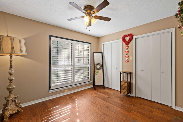 unfurnished bedroom featuring a textured ceiling, hardwood / wood-style flooring, ceiling fan, and multiple closets