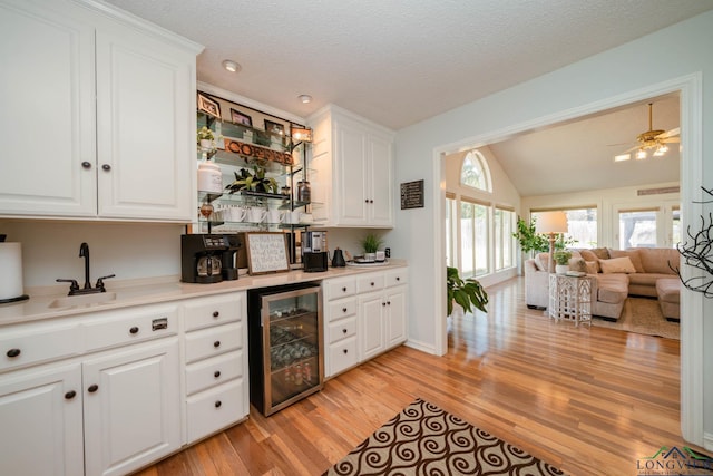 kitchen with beverage cooler, lofted ceiling, light wood-style flooring, light countertops, and white cabinetry