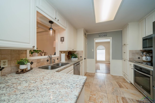 kitchen featuring light stone countertops, wainscoting, white cabinets, stainless steel appliances, and a sink