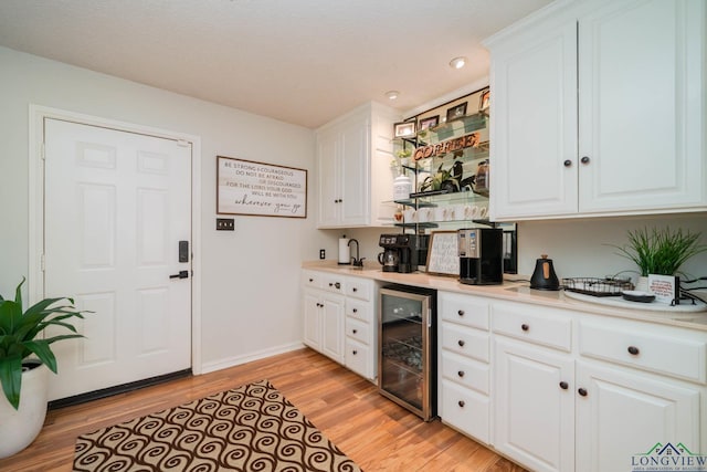 kitchen with light countertops, white cabinets, beverage cooler, and light wood finished floors