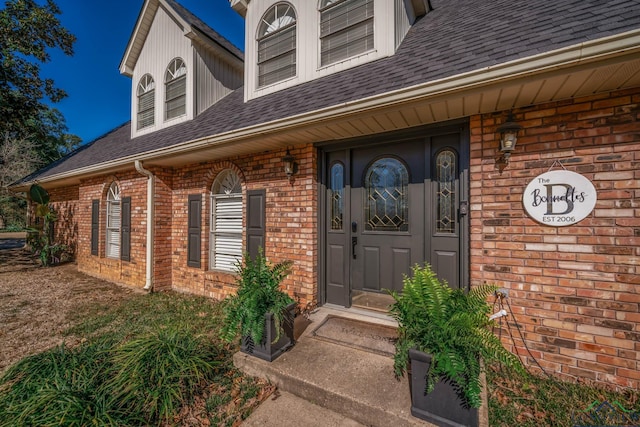 doorway to property with brick siding and roof with shingles