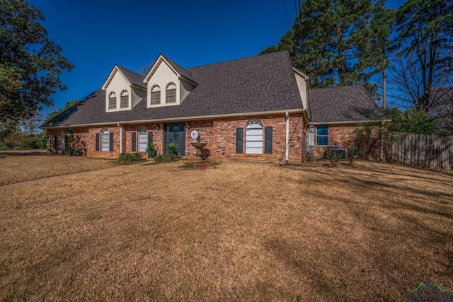 cape cod home with a front yard, fence, brick siding, and roof with shingles