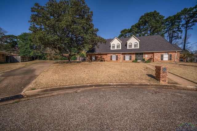 cape cod house with brick siding, a shingled roof, a front lawn, and fence