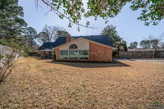 back of house with a gazebo, a fenced backyard, brick siding, and a chimney